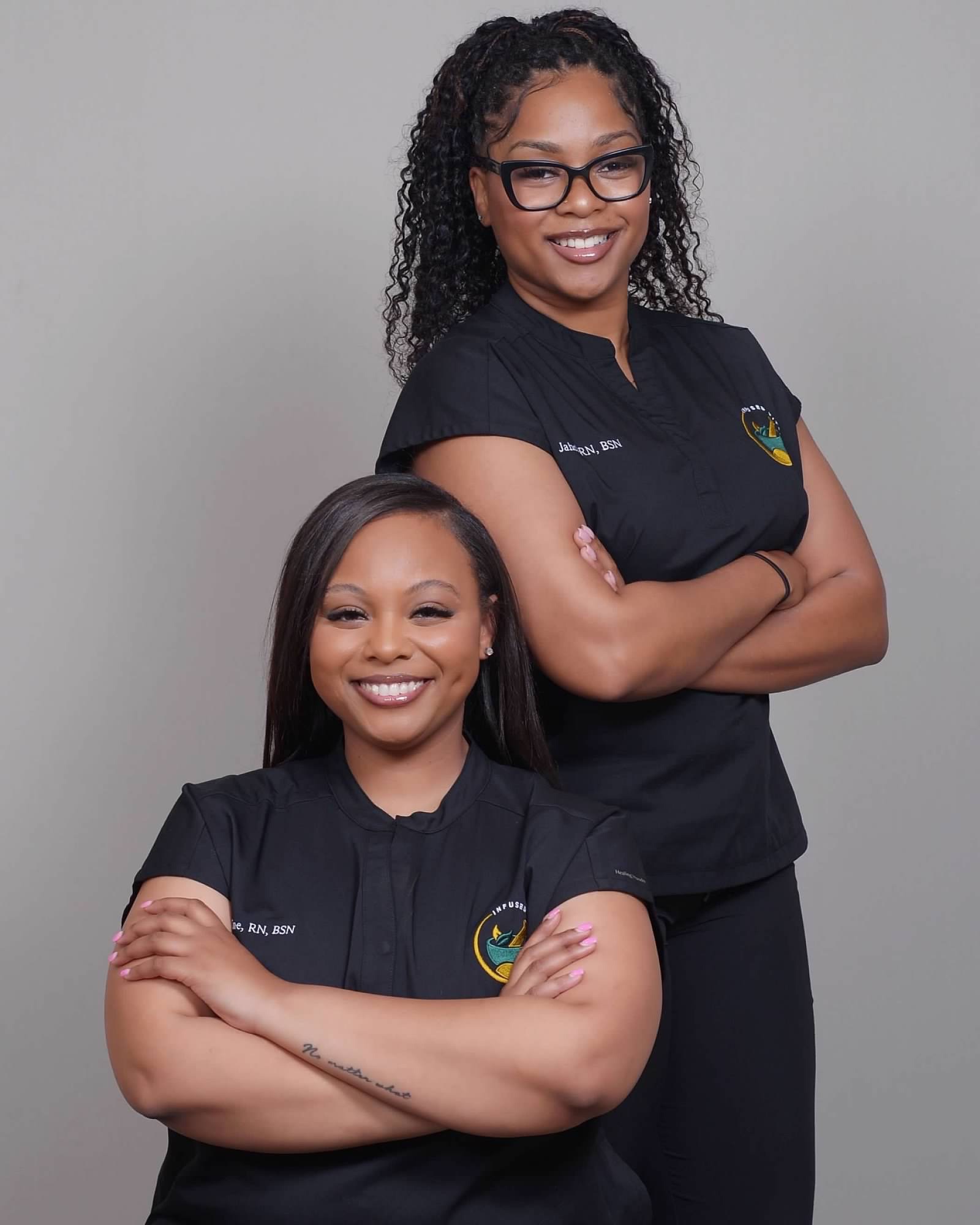 Two healthcare professionals in black scrubs smiling with arms crossed